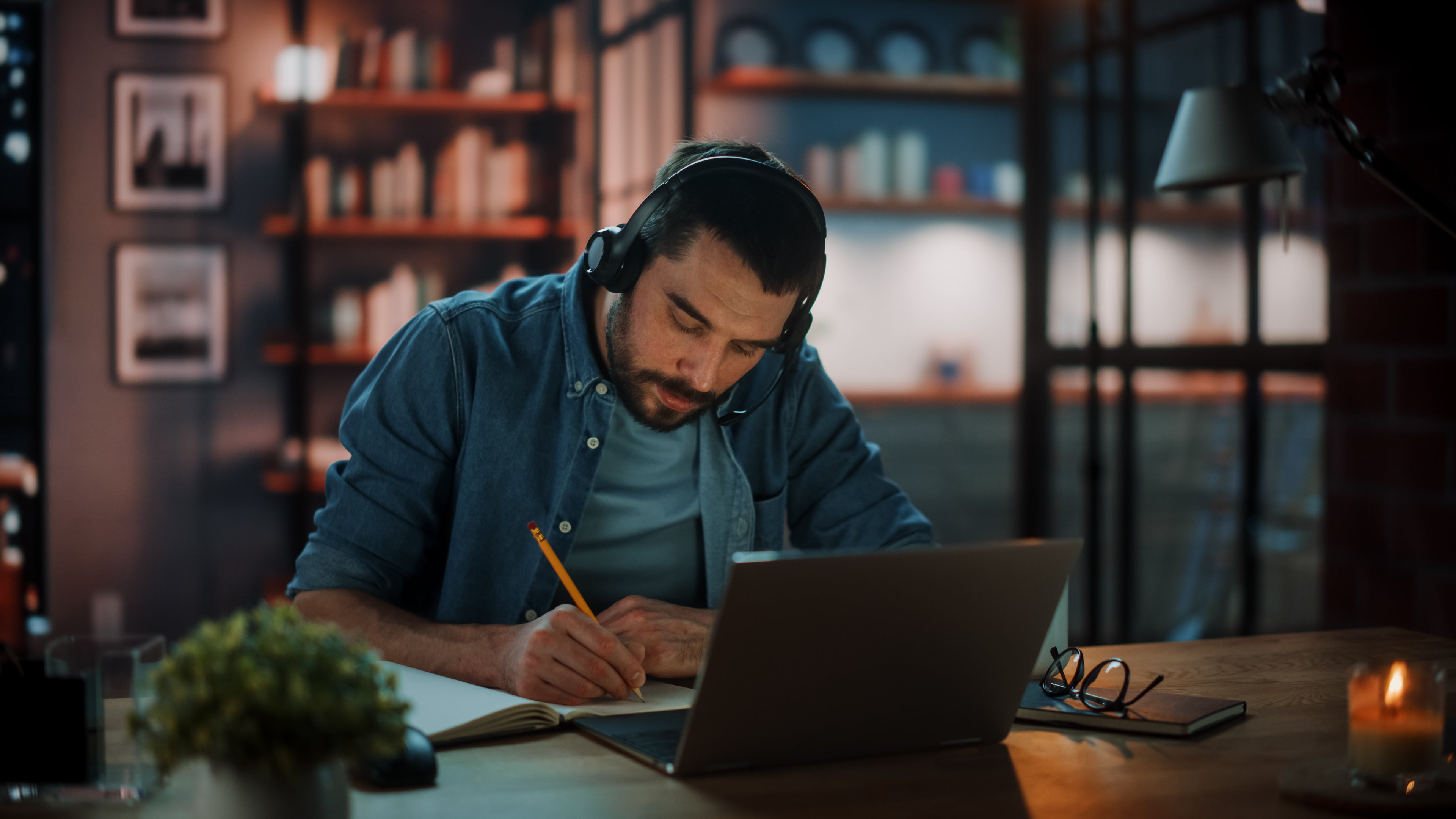 Man taking notes in front of laptop, while wearing headphones. A very calm atmosphere.